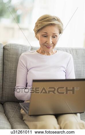 Senior woman sitting on sofa and using laptop View Large Photo Image Stock Image - Senior woman sitting on sofa and using laptop. Fotosearch