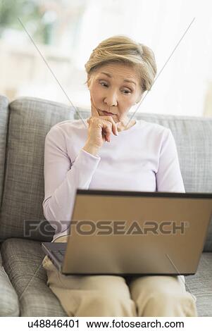 Senior woman sitting on sofa and using laptop View Large Photo Image Stock Image - Senior woman sitting on sofa and using laptop. Fotosearch
