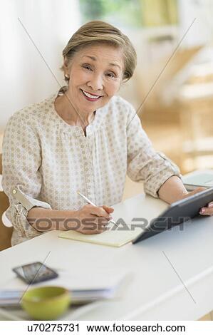 Stock Image - Senior woman using tablet pc at home. Fotosearch