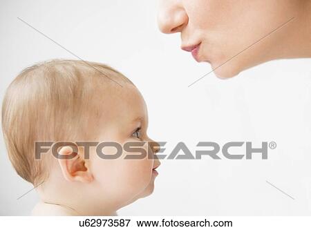 Stock Photo - Side view of mother about to kiss her baby daughter (6-11 months). Fotosearch
