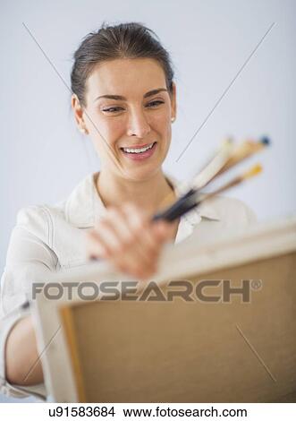 Picture - Studio Shot of woman holding paintbrushes and artist's canvas. Fotosearch