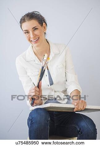 Studio Shot of woman sitting on stool, holding paintbrushes and artist's canvas View Large Photo Image Stock Image - Studio Shot of woman sitting on stool, holding paintbrushes and artist's canvas. Fotosearch