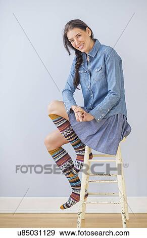 Stock Photo - Studio Shot of woman sitting on stool wearing striped kneesocks. Fotosearch