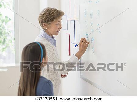 Stock Image - Teacher and schoolgirl (8-9) writing at whiteboard. Fotosearch