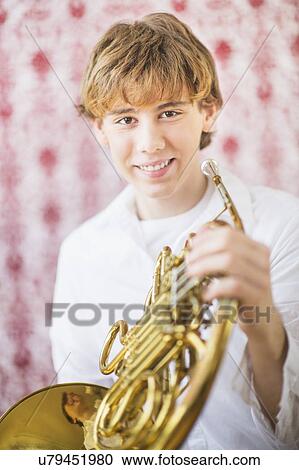 Stock Image - Teenage boy (14-15) holding french horn. Fotosearch
