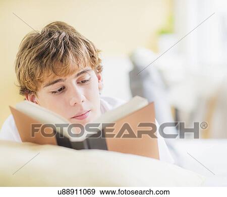 Teenage boy (14-15) lying on bed and reading book View Large Photo Image Stock Photo - Teenage boy (14-15) lying on bed and reading book. Fotosearch