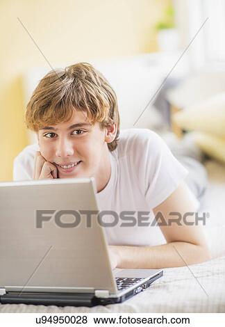 Teenage boy (14-15) lying on bed and using laptop View Large Photo Image Stock Photo - Teenage boy (14-15) lying on bed and using laptop. Fotosearch