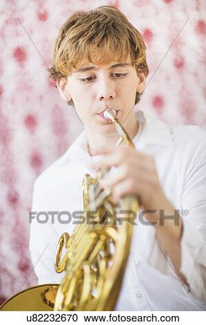 Stock Image - Teenage boy (14-15) playing french horn. Fotosearch