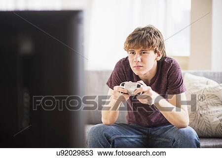 Stock Image - Teenage boy (14-15) playing video game. Fotosearch