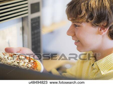 Stock Image - Teenage boy (14-15) preparing pizza. Fotosearch