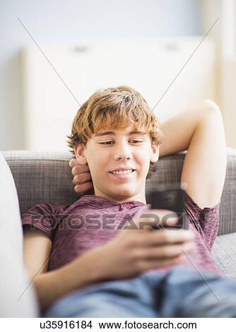 Picture - Teenage boy (14-15) sitting and text messaging. Fotosearch
