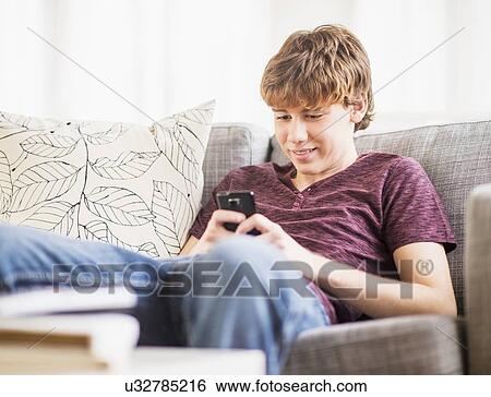 Stock Photograph - Teenage boy (14-15) sitting and text messaging. Fotosearch