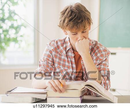 Stock Photography - Teenage boy (14-15) sitting in classroom with pencil and books. Fotosearch