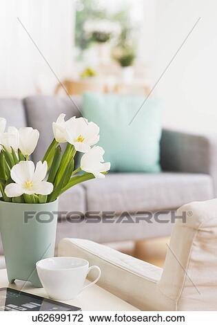 Stock Image - Vase with flowers and digital tablet on coffee table by sofa. Fotosearch