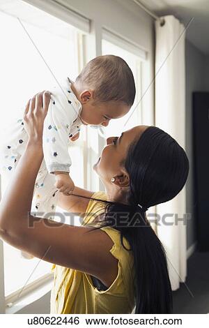 Stock Photograph - Woman holding up her baby son (2-5 months). Fotosearch