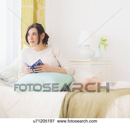 Woman leaning against pillow in bed, Holding book and looking away View Large Photo Image Stock Photo - Woman leaning against pillow in bed, Holding book and looking away. Fotosearch