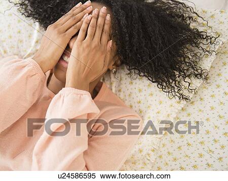 Stock Photography - Woman lying down on bed, covering face with her hands. Fotosearch