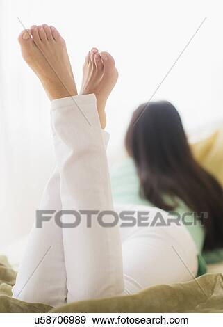 Stock Photo - Woman lying down on bed, Rear view. Fotosearch