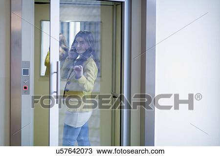 Woman opening glass door and talking on cell phone View Large Photo Image Stock Image - Woman opening glass door and talking on cell phone. Fotosearch