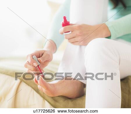 Stock Photograph - Woman sitting on bed and polishing toe nails. Fotosearch