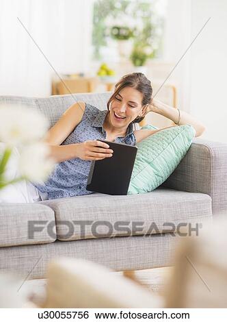 Stock Photograph - Woman using tablet pc on sofa. Fotosearch