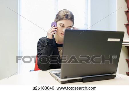 Woman working on laptop and talking on cell phone View Large Photo Image Stock Photograph - Woman working on laptop and talking on cell phone. Fotosearch