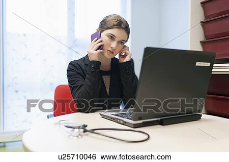 Stock Photograph - Woman working on laptop and talking on cell phone. Fotosearch