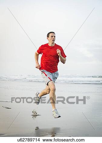 Picture - Young adult man running on beach. Fotosearch