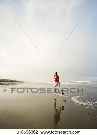 Stock Image - Young adult man running on beach. Fotosearch