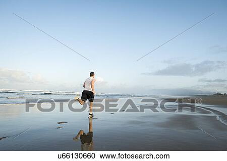 Stock Image - Young adult man running on beach. Fotosearch