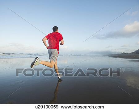 Stock Photo - Young adult man running on beach. Fotosearch