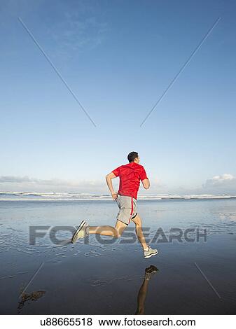 Stock Photo - Young adult man running on beach. Fotosearch