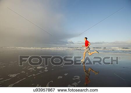 Stock Photo - Young adult man running on beach. Fotosearch