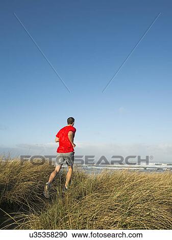 Stock Image - Young adult man running on dune. Fotosearch