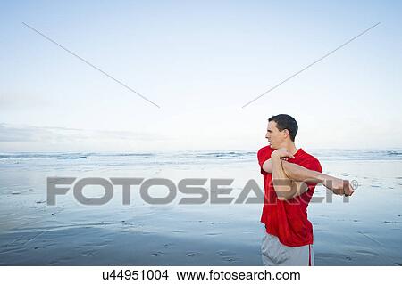 Picture - Young adult man stretching on beach. Fotosearch