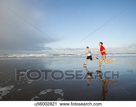 Stock Image - Young adult men running on beach. Fotosearch