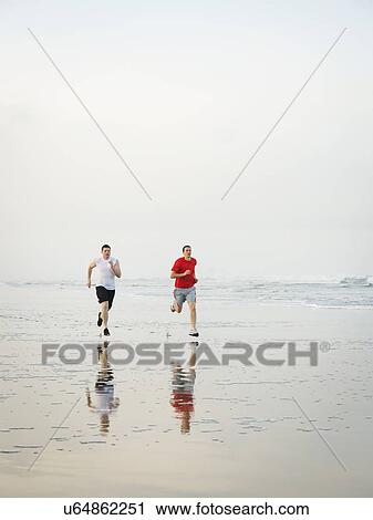 Stock Image - Young adult men running on beach. Fotosearch