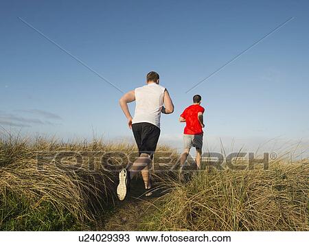Stock Image - Young adult men running on dune. Fotosearch