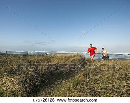 Stock Photograph - Young adult men running on dune. Fotosearch