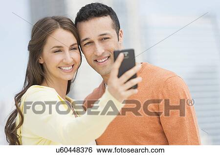 Young couple photographing themselves with mobile phone View Large Photo Image Stock Photograph - Young couple photographing themselves with mobile phone. Fotosearch