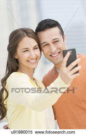 Young couple photographing themselves with mobile phone View Large Photo Image Stock Photography - Young couple photographing themselves with mobile phone. Fotosearch