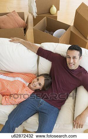 Stock Image - Young couple resting on sofa after moving into new home. Fotosearch