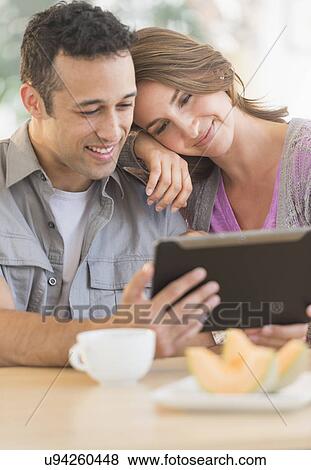 Stock Photo - Young couple using digital tablet at kitchen table. Fotosearch