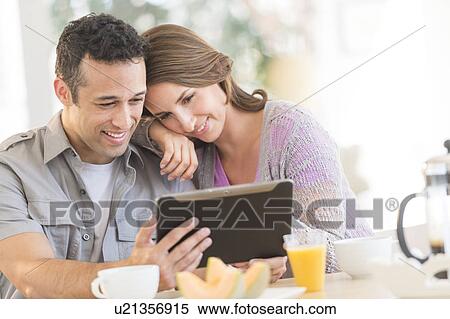 Stock Photography - Young couple using digital tablet at kitchen table. Fotosearch