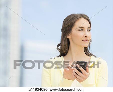 Stock Image - Young woman photographing herself with mobile phone. Fotosearch