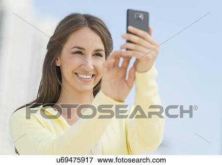 Young woman photographing herself with mobile phone View Large Photo Image Stock Photo - Young woman photographing herself with mobile phone. Fotosearch