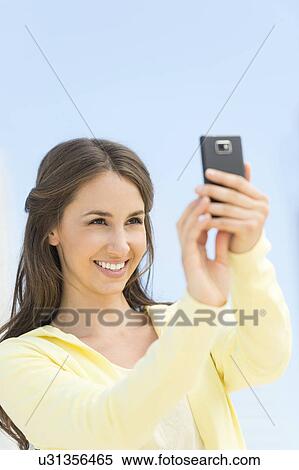 Stock Photography - Young woman photographing herself with mobile phone. Fotosearch