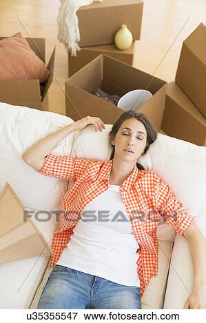 Stock Photo - Young woman resting on sofa after moving into new home. Fotosearch