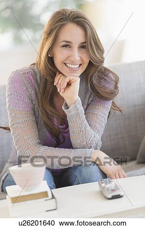 Stock Image - Young woman sitting on sofa. Fotosearch