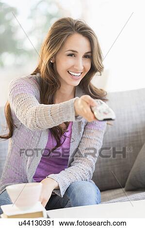 Stock Image - Young woman watching tv on sofa. Fotosearch